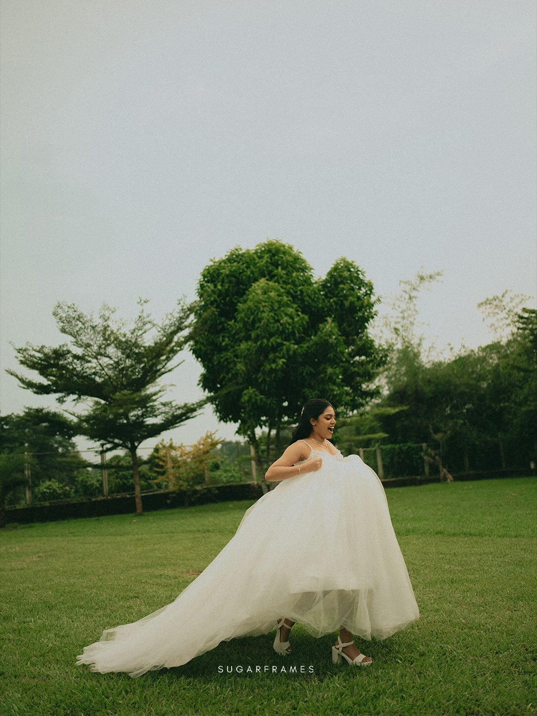 A joyful bride lifting her wedding dress in a green garden