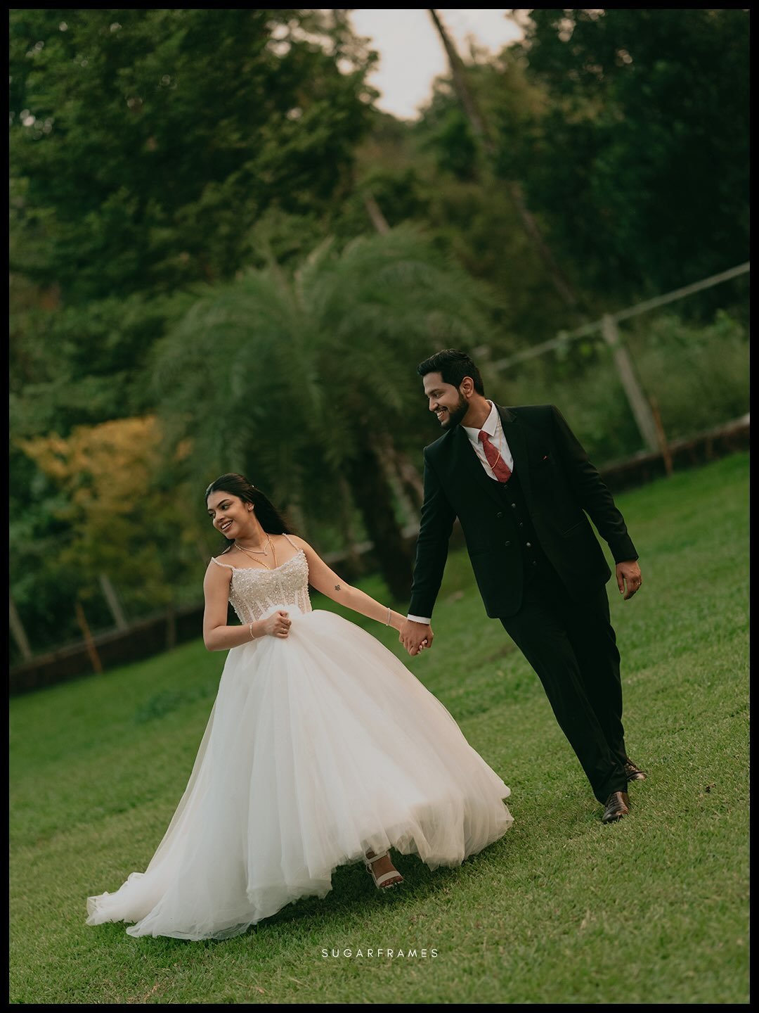 A newlywed couple walking hand in hand through a green garden