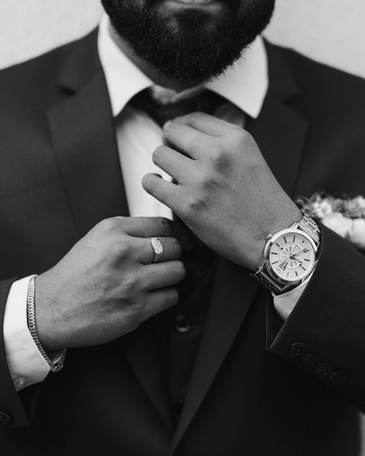 A groom adjusting his tie in a black-and-white portrait
